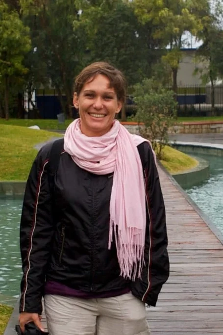 Kristiina Isabelle Nimmo, founder of UnderWorks, smiling while walking on a stone path near a water feature in a green public space.