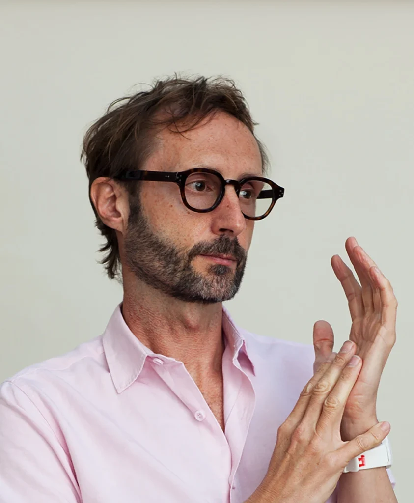 A portrait of Peter Culley, an architect and urban regeneration specialist, looking thoughtfully to the side while wearing a pink shirt and tortoiseshell glasses.